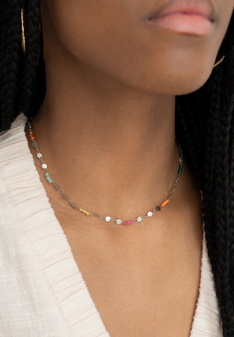 Collier en perles colorées avec des accents circulaires métalliques, comportant des perles orange, rose, jaune, verte et bleue sur une chaîne argentée.