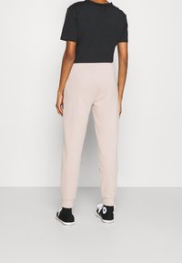 Graues, kurzes T-Shirt kombiniert mit hellrosa, schmal zulaufenden Jogginghosen, die elastische Bündchen, Seitentaschen und schwarze Sneakers mit weißen Akzenten aufweisen.