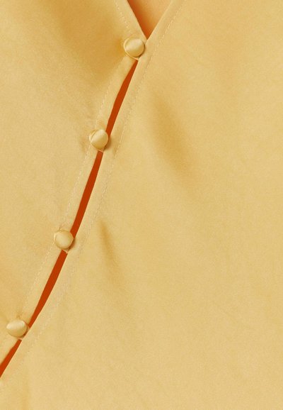 Tessuto giallo con quattro bottoni rotondi rivestiti in tessuto fissati lungo una cucitura verticale, che mostrano cuciture dettagliate.