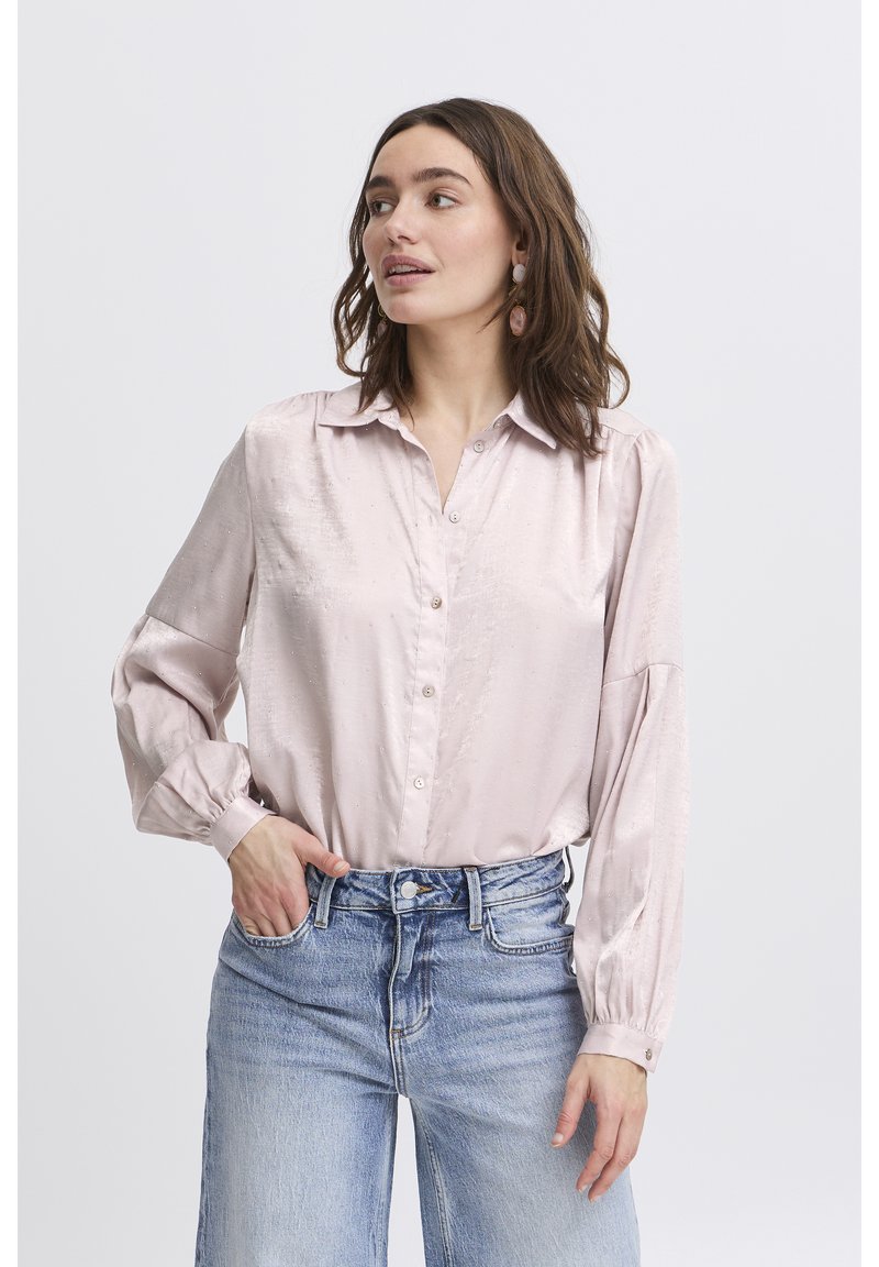 Light pink satin blouse with a button-up front, collared neck, long puff sleeves, and textured accents. Paired with high-waisted jeans.