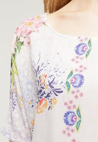 Floral-patterned blouse with a round neckline. Features colorful flowers in pink, purple, and orange on a light background with subtle texture.