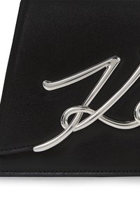 Borsa nera in pelle con accenti in hardware argento lucido in un design corsivo, che mette in evidenza dettagli intricati e una superficie liscia.