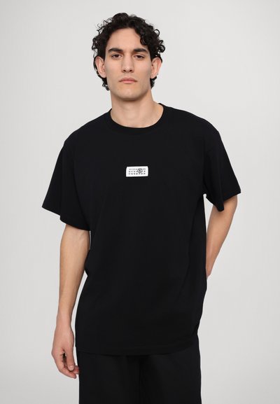 T-shirt en coton noir à manches courtes et col rond. Présente une petite étiquette graphique blanche au centre devant. Coupe classique.