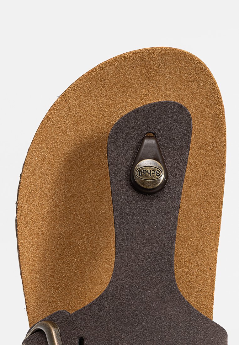 Semelle en cuir brun avec une texture en daim marron clair, présentant une sangle brun foncé et un accent de logo métallique rond.