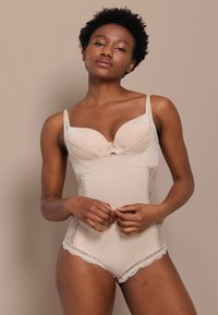 Body beige con rifiniture in pizzo, coppe imbottite, spalline regolabili e una texture liscia. Orlo inferiore con bordi a ondina.