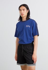 T-shirt en coton bleu marine à manches courtes, avec un logo imprimé blanc. Associé à un short en mesh noir, souligné par des rayures blanches.