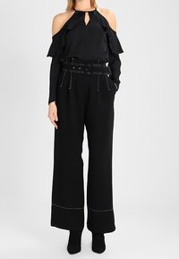 Top noir à épaules dénudées avec des manches volantes et un détail en trou de serrure, associé à un pantalon noir à jambe large avec une taille ceinturée et des coutures blanches.