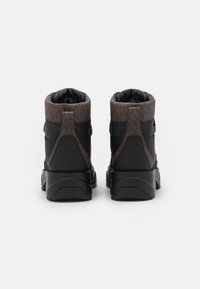 Bottes de randonnée noires avec un col en textile à motifs bruns, une semelle épaisse et un design épuré. Présente une finition mate et un matériel minimal.