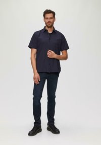 Korte mouwen, marineblauw geruit shirt van geweven stof, gecombineerd met donkere jeans en zwarte veterschoenen. Voorzien van een button-down kraag.