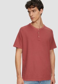 Rode katoenen t-shirt met korte mouwen, ronde hals en drieknopenbies. Heeft een gestructureerde stof en een relaxte pasvorm.