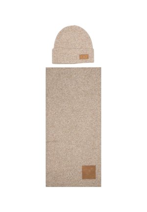 Beanie in maglia beige con risvolto e etichetta in pelle, abbinato a una sciarpa rettangolare coordinata con una texture e un'etichetta simili.