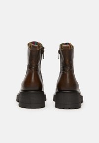 Botas de tobillo de cuero marrón con suela negra gruesa, con una cremallera a cada lado y un forro de tela colorido en el interior.