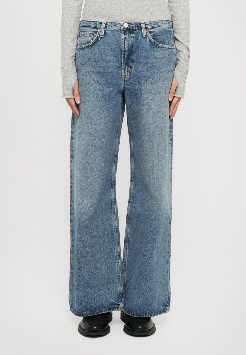 Light blue wide-leg jeans with a mid-rise waist, five pockets, noticeable fading, and stitched details. Worn with black shoes.