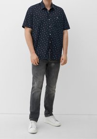 Camicia corta blu con motivo floreale bianco, colletto a bottoni, taschino sul petto; abbinata a jeans grigi e sneaker bianche.
