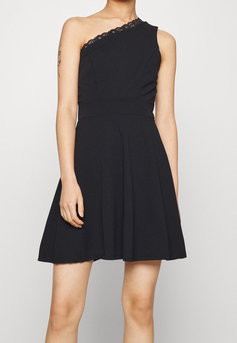 Černé šaty bez rukávů s jedním ramenem, zdobené krajkovými detaily kolem výstřihu a s rozšířeným designem sukně. Hladká textura látky.