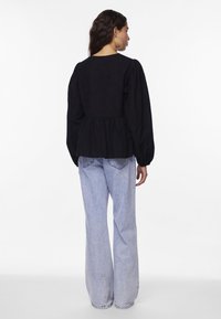 Svart långärmad blus med peplum midja, rund halsringning och rynkade ärmar, kombinerad med ljusblå utsvängda jeans.