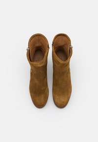 Botines de ante en amarillo mostaza con una textura suave. Presentan una cremallera lateral y un tacón ligero. El interior está forrado con un material suave en color marrón claro.