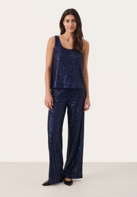 Marineblaues, paillettenbesetztes Zweiteiler-Outfit mit einem ärmellosen Oberteil und weit geschnittenen Hosen. Der Stoff hat eine glänzende Oberfläche und reflektiert das Licht, was für funkeln sorgt.