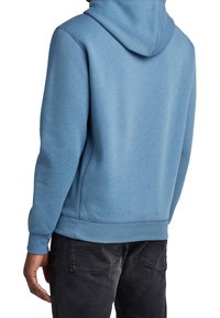 Haut à capuche bleu clair en tissu doux, doté d'une capuche avec cordon de serrage, de poignets et d'un ourlet côtelés, avec une coupe décontractée et un minimum de détails de couture.