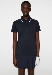 Navyblaues Poloshirt mit weißem Kragen und Knopfleiste, mit strukturierten Seitenpaneelen. Kombiniert mit einem passenden plissierten Rock.