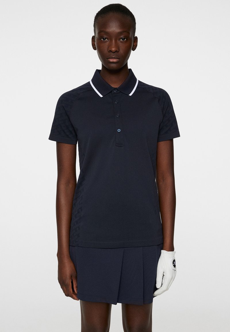 Navyblaues Poloshirt mit weißem Kragen und Knopfleiste, mit strukturierten Seitenpaneelen. Kombiniert mit einem passenden plissierten Rock.