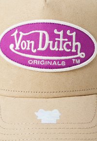 Casquette beige en tissu texturé, avec un patch ovale violet et une broderie blanche qui lit "Von Dutch ORIGINALS TM."