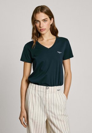 Donkergroene v-hals t-shirt gemaakt van zachte stof, met een klein wit logo op de linkerborst, gecombineerd met lichtgestreepte, hoge taille broek.