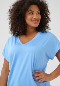 Light blue V-neck top with short sleeves, made of soft, smooth fabric. The design features a relaxed fit and understated stitching details.
