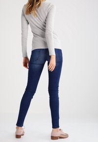 Grå långärmad topp i kombination med mörkblå smala jeans. Jeansna har bakfickor och en åtsittande passform som kompletteras av beige skor.