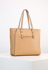 Sac fourre-tout en cuir beige avec deux poignées, une forme structurée et des accents en métal argenté. Il dispose d'une poche avant.