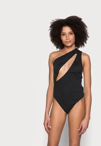 Costume da bagno intero nero con spallina singola e ritaglio laterale. Tessuto liscio, gambe alte e design minimalista.