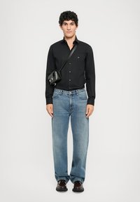 Črna srajca z gumbi, ohlapne svetlo modre jeans hlače, črna torba čez telo in temna obutev. Preprost dizajn z vsakodnevnim krojem.