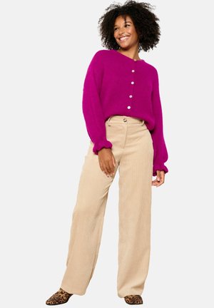 Fuchsia gebreide cardigan met ronde hals en knoopsluiting, gecombineerd met brede beige corduroy broek. Opvallende schoenen met luipaardprint.