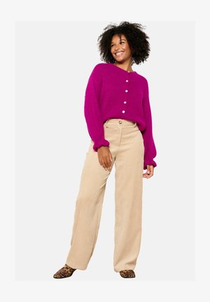 Cárdigan de punto fucsia con cuello redondo y cierre de botones, combinado con pantalones de pana anchos en color beige. Notables zapatos de estampado de leopardo.