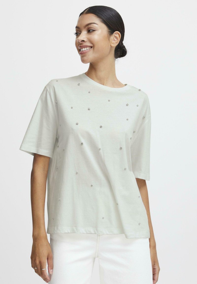 T-shirt verde chiaro con maniche corte, scollatura tonda e decorazioni argentate sparse sul davanti. Materiale in cotone morbido con vestibilità rilassata.