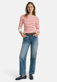 Rot und weiß gestreifter Strickpullover mit langen Ärmeln, kombiniert mit hellblauen geraden Jeans und marineblauen Slippern. Brauner Gürtel als Akzent.
