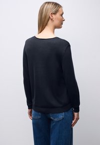Czarny sweter z długimi rękawami i okrągłym dekoltem, o gładkiej fakturze i prążkowanym brzegu, zestawiony z niebieskimi dżinsami.
