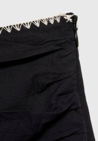 Tessuto nero con texture arricciata, chiusura con zip e cuciture a contrasto nella parte superiore. Materiale liscio e leggero.