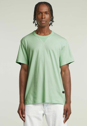Lichtgroene katoenen T-shirt met korte mouwen, ronde halslijn en een subtiele V-detail. Beschikt over een klein merkteken aan de zoom.