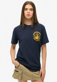 Camiseta de algodón azul marino con cuello redondo y mangas cortas. Logo amarillo impreso con texto en el frente. Textura suave.