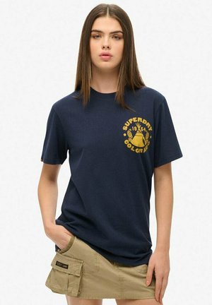 T-shirt en coton bleu marine avec un col rond et des manches courtes. Logo jaune imprimé avec du texte sur le devant. Texture lisse.