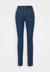 Jean denim bleu foncé à jambes droites, vu de dos, avec deux poches arrière et une étiquette à la ceinture.
