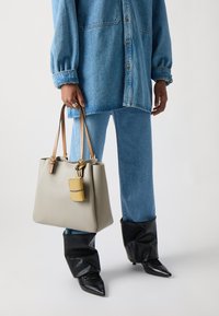 Pelēka ādas rokassoma ar brūniem siksnām, ar dzeltenu akcents. Valkāta kopā ar zilu denimu apģērbu un melniem smailiem zābakiem.