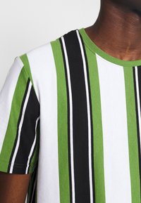 Koszulka w paski w kolorach zielonym, czarnym i białym. Wykonana z bawełny, z okrągłym dekoltem i krótkimi rękawami. Miękka tekstura, casualowy design.