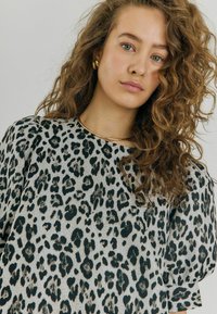 Leopardmönstrad topp med en grå bakgrund och svarta fläckar, mjuk textur, rund halsringning och korta puffärmar.