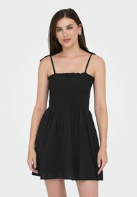 Robe noire avec corsage smocké, encolure à volants et fines bretelles réglables. Jupe évasée en tissu léger.