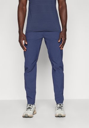 Navy blue trousers with a slim fit, featuring a smooth texture, two front pockets, and a tapered leg design. Combined with gray and beige shoes.