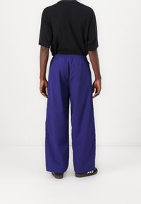 Violet leveled pants with an elastic waistband and side pockets, paired with a black short-sleeve shirt. Smooth fabric texture.