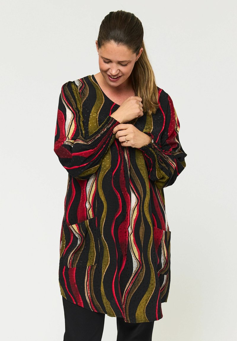 Lang tunika med et bølgende mønster i sort, rød, guld og grøn. Den har lange ærmer, V-udskæring og to forlommer.