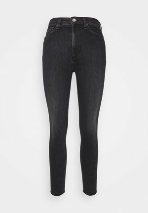 Vyötäröltä korkeavyötäröiset mustat kapeat farkut, joissa edessä nappi- ja vetoketjusuljin, edessä ja takana taskut, esitetty yksinkertaisen taustan edessä.